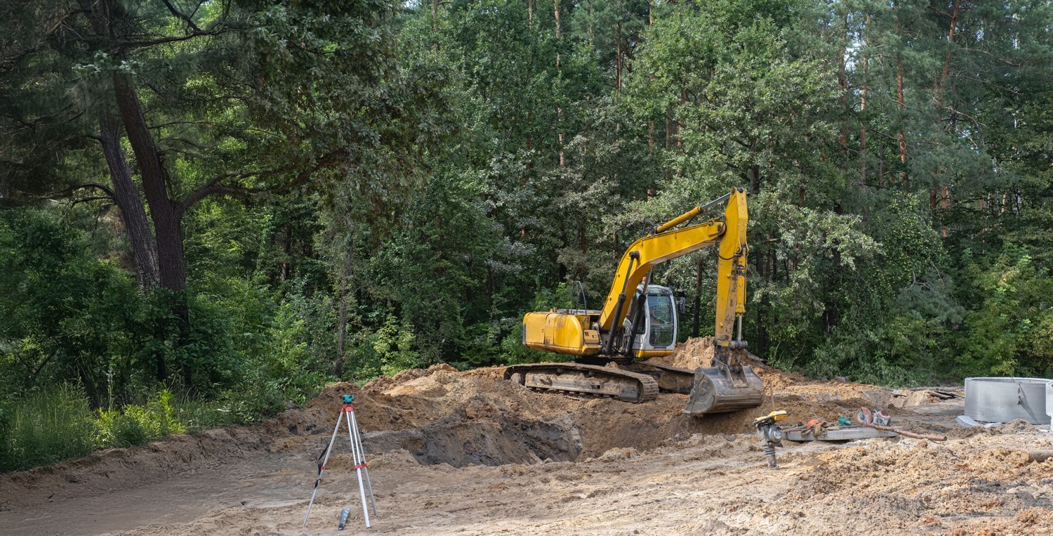 Aerial view of an excavator working exposed ground at a woodland site edge
