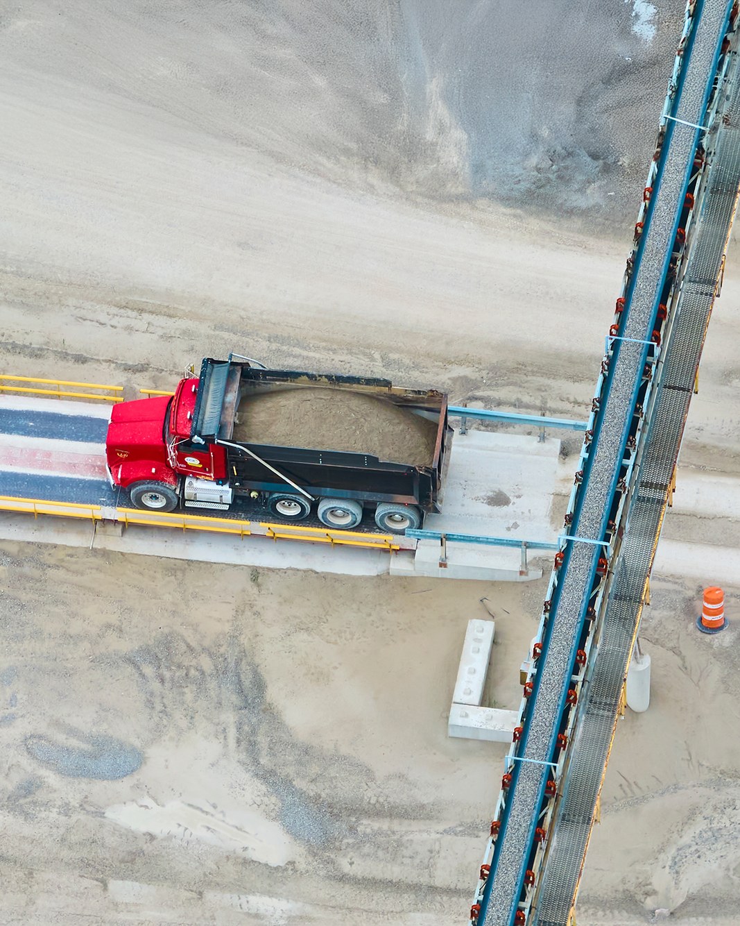 Aerial view of a haul truck on a weighbridge beside a conveyor at a resource recovery facility